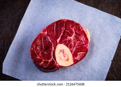 Raw osso buco steak lies on waxpaper. Top down view of fresh veal shank meat cut with marrow bone