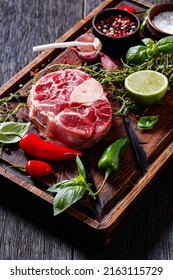raw osso buco, veal shank steak on wood rustic cutting board with peppercorns, fresh thyme, chili  peppers,  garlic and lime, vertical view