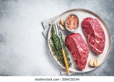 Raw Oyster Top Blade Or Flat Iron Roast Beef Meat Steaks On A Plate With Herbs. White Background. Top View. Copy Space