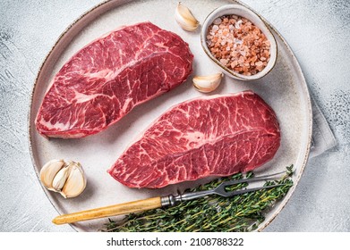 Raw Oyster Top Blade Or Flat Iron Roast Beef Meat Steaks On A Plate With Herbs. White Background. Top View