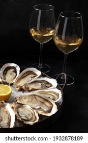Raw oysters on a platter with glasses of white wine on a black background