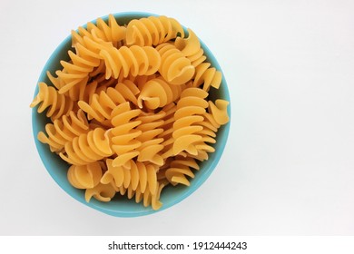 Raw pasta fusilli in blue bowl on white background. Healthy food ingredients on the kitchen table. Overhead view, copy space, selective focus - Powered by Shutterstock