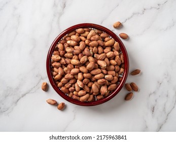 Raw peanut seeds in a wooden bowl on a marble countertop. Dried peeled groundnut as healhy vegetarian snack. Whole organic monkey nut for dietary nutrition. Arachis hypogaea fruits. Top view.