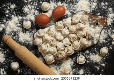 Raw pelmeni, top view, flat lay. Cooking pelmeni, flour, eggs and wooden rolling pin. Meat dumplings or ravioli on wooden board, dark table. Slavic traditional dish. Food background - Powered by Shutterstock