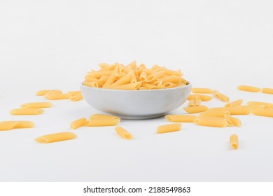 Raw penne pasta in ceramic bowl with other penne pasta scatter around eye level angle - Powered by Shutterstock