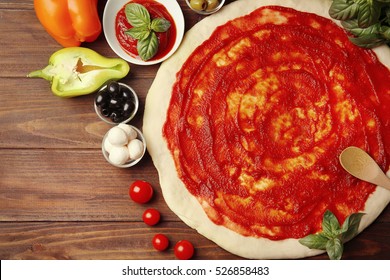 Raw Pizza Dough With Sauce And Ingredients On Wooden Table