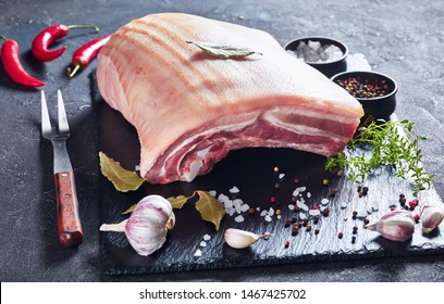 raw pork belly with skin on a black slate tray with spices and herbs, horizontal view from above, close-up - Shutterstock ID 1467425702