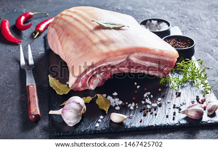 raw pork belly with skin on a black slate tray with spices and herbs, horizontal view from above, close-up