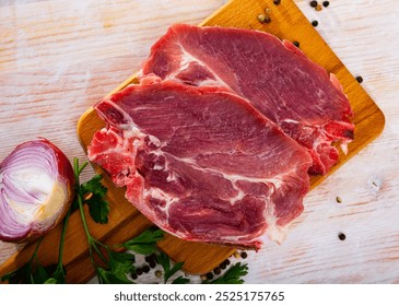 Raw pork chops served on wooden board with purple onion, parsley and black pepper - Powered by Shutterstock