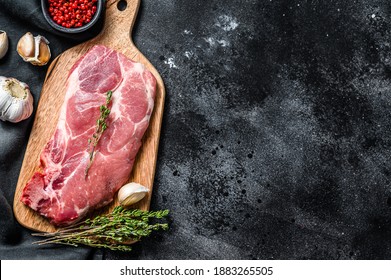 Raw pork cutlet steak. Piece of raw meat ready for preparation with greens and spices. Black background. Top view. Copy space