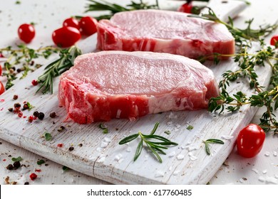 Raw Pork Loin chops on a cutting board with herbs, rosemary, thyme, chilli, salt, pepper on white cutting board. - Shutterstock ID 617760485