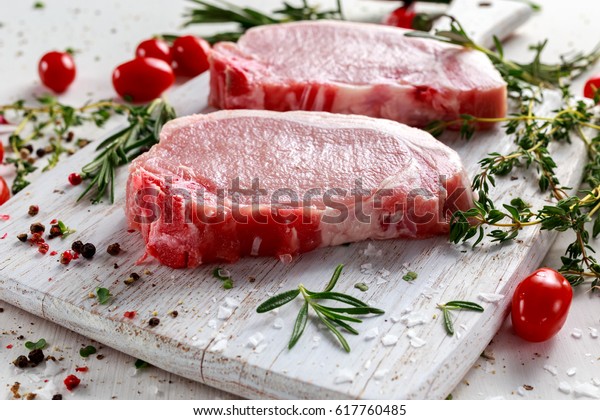 Raw Pork\
Loin chops on a cutting board with herbs, rosemary, thyme, chilli,\
salt, pepper on white cutting\
board.