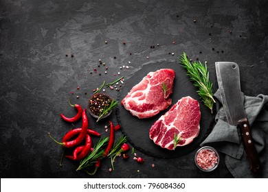 Raw pork meat. Fresh steaks on slate board on black background. Top view