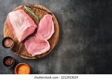 Raw pork meat on wooden board on grey background  with rosemary, salt and pepper. Pork loin. Copy space. Top view.