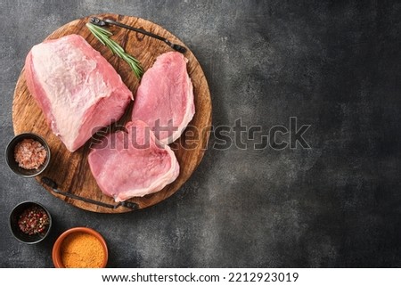 Raw pork meat on wooden board on grey background  with rosemary, salt and pepper. Pork loin. Copy space. Top view.