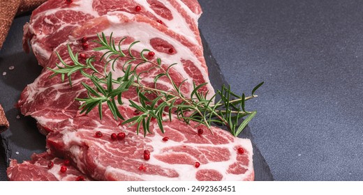 Raw pork neck meat. Chop steak, red peppercorn, garlic cloves, sea salt and fresh rosemary. Trendy stand, black background, flat lay, banner format - Powered by Shutterstock