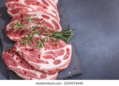 Raw pork neck meat. Chop steak, red peppercorn, garlic cloves, sea salt and fresh rosemary. Trendy stand, black background, flat lay, top view - Powered by Shutterstock