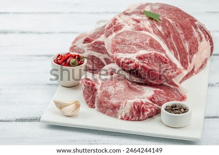 Raw pork neck meat. Traditional ingredients for cooking food. Garlic cloves, fresh parsley. Trendy stand, white background, flat lay, copy space