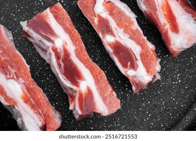 Raw pork ribs displayed on a black surface, ideal for grilling or smoking. - Powered by Shutterstock