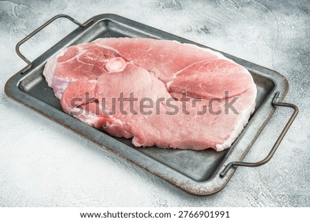 Raw pork shoulder joint with bone on metal pan grey background fresh meat cut for slow cook barbecue pulled pork and cuisine.