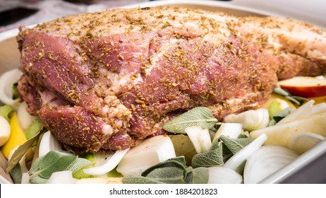 A Raw Pork Shoulder Roast Lies In A Baking Dish Together With Apples, Onions, Sage And Cider. The Roast Is Rubbed With Fennel Seeds, Salt And Chilli.