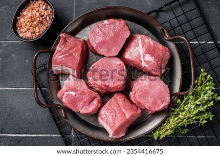 Raw pork tenderloin medallions steaks on a kitchet tray with thyme and sea salt. Black background. Top view.