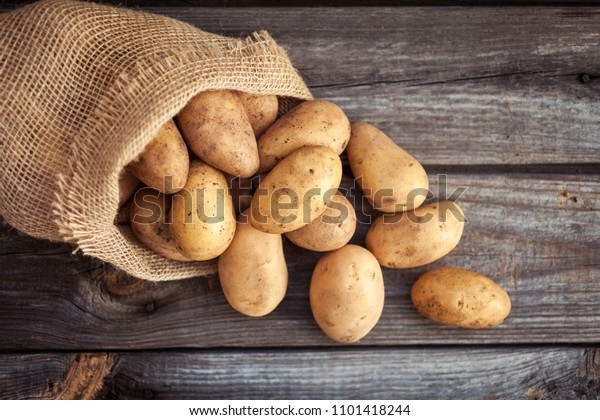 Raw potato food . Fresh potatoes in an old sack\
on wooden background. Top\
view