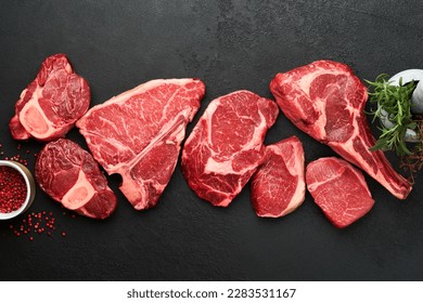 Raw prime steaks. Variety of fresh black angus prime meat steaks T-bone, New York, Ribeye, Striploin, Tomahawk cutting board on black or dark background. Set of various classic steaks. Top view.  - Powered by Shutterstock