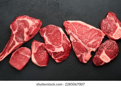 Raw prime steaks. Variety of fresh black angus prime meat steaks T-bone, New York, Ribeye, Striploin, Tomahawk cutting board on black or dark background. Set of various classic steaks. Top view. 
