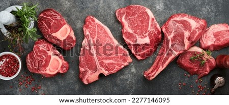Raw prime steaks. Variety of fresh black angus prime meat steaks T-bone, New York, Ribeye, Striploin, Tomahawk on black or gray stone background. Set of various classic steaks. Top view, copy space.