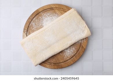 Raw puff pastry dough on white tiled table, top view