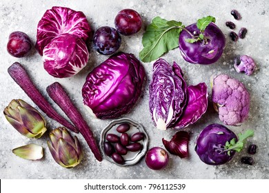 Raw purple vegetables over gray concrete background. Cabbage, radicchio salad, olives, kohlrabi, carrot, cauliflower, onions, artichoke, beans, potato, plums. Top view, flat lay.  - Powered by Shutterstock