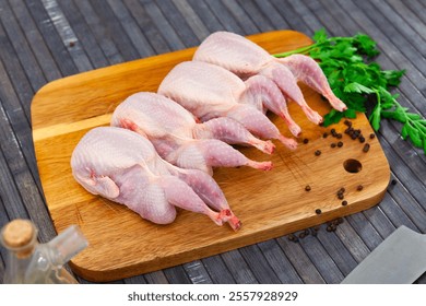 Raw quails on wooden cutting board with parsley stems and peppercorns.