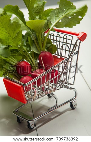 Raw radishes, shopping cart on a white wooden background
