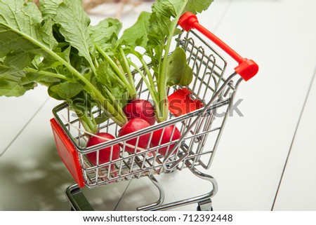 Raw radishes, shopping cart on a white wooden background
