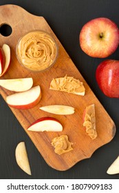 Raw Red Apples And Peanut Butter On A Rustic Wooden Board On A Black Background, Top View. Flat Lay, Overhead, From Above.