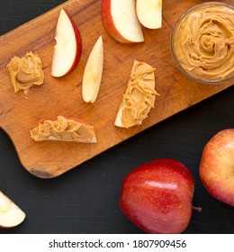 Raw Red Apples And Peanut Butter On A Rustic Wooden Board On A Black Surface, Top View. Flat Lay, Overhead, From Above.