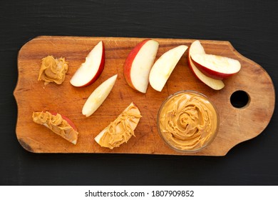 Raw Red Apples And Peanut Butter On A Rustic Wooden Board On A Black Background, Top View. Flat Lay, Overhead, From Above. 