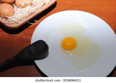 Raw Red Chicken Eggs On A Plate. You Can See The Tip Of A Wooden Spoon