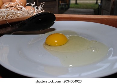 Raw Red Chicken Eggs On A Plate. You Can See The Tip Of A Wooden Spoon