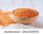 Raw red lentils are scattered out of the wooden bowl on a light table, selective focus.