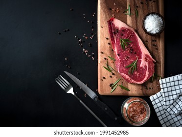 raw ribeye beef steak with Himalayan Pink salt, rosemary leaf herbs, and spices black pepper on a wooden cutting board. Top view on a dark background with copy space for your text - Powered by Shutterstock