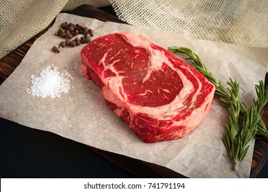 raw ribeye steak lying on Kraft paper around the pepper, salt, rosemary on a wooden Board - Shutterstock ID 741791194