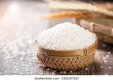 Raw Rice In A Bamboo Basket With Wheat On Wooden Background
