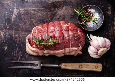 Raw roast beef Rump, seasonings and meat fork on dark metal background