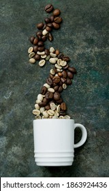 Raw And Roasted Coffee Beans Shaped In Form Of Smoke  Coming From White Cupover A Metal Background. Racial Inclusion Concept. Top View.  Flat Lay