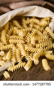 Raw rotini or fusilli pasta in bag, photographed on rustic wood (Selective Focus, Focus on the rotinis at the opening of the bag)
