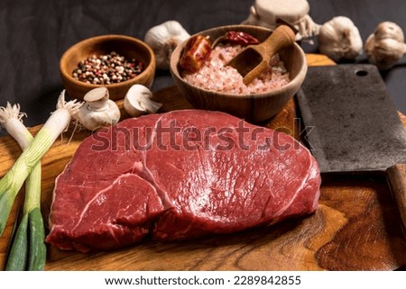 Raw rump beef cut or top sirloin meat steak on butcher table. Black background. Preparation of grilling. Quality beef. Barbecue season.