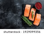 Raw salmon fillet steaks on marble board with herbs. Black background. Top view. Copy space.