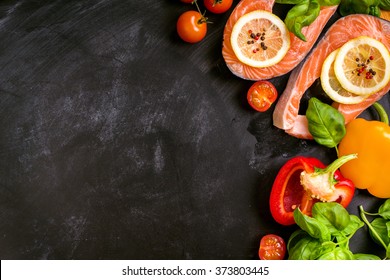 Raw salmon steaks and fresh ingredients for cooking on a dark background. Banner, frame, menu. Healthy and diet food concept. Space for text. Top view - Powered by Shutterstock